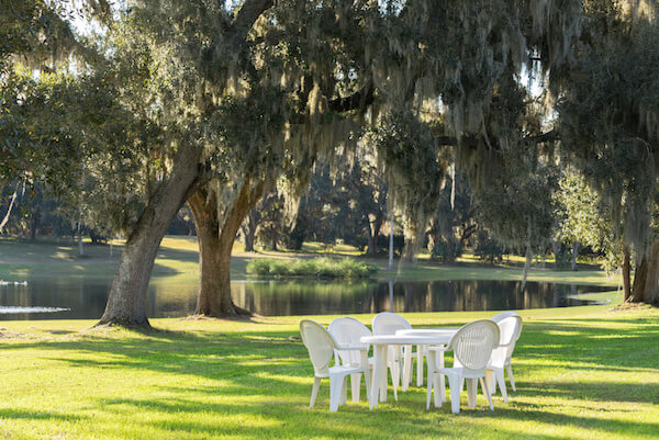 White plastic table and chairs outside in a garden on green lawn by a pond or lake in the afternoon sun and a peaceful relaxing serene tranquil setting